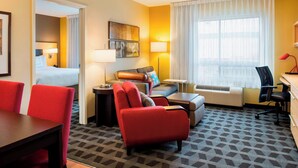 A hotel room with a bed, a sofa, a desk, and a chair. There is a window with curtains, a lamp, and a picture on the wall. - Towneplace Suites by Marriott Red Deer (Red Deer)