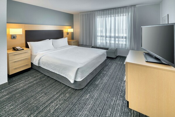 A hotel room with a large bed, bedside tables with lamps, a flat-screen TV, and a large window with curtains.