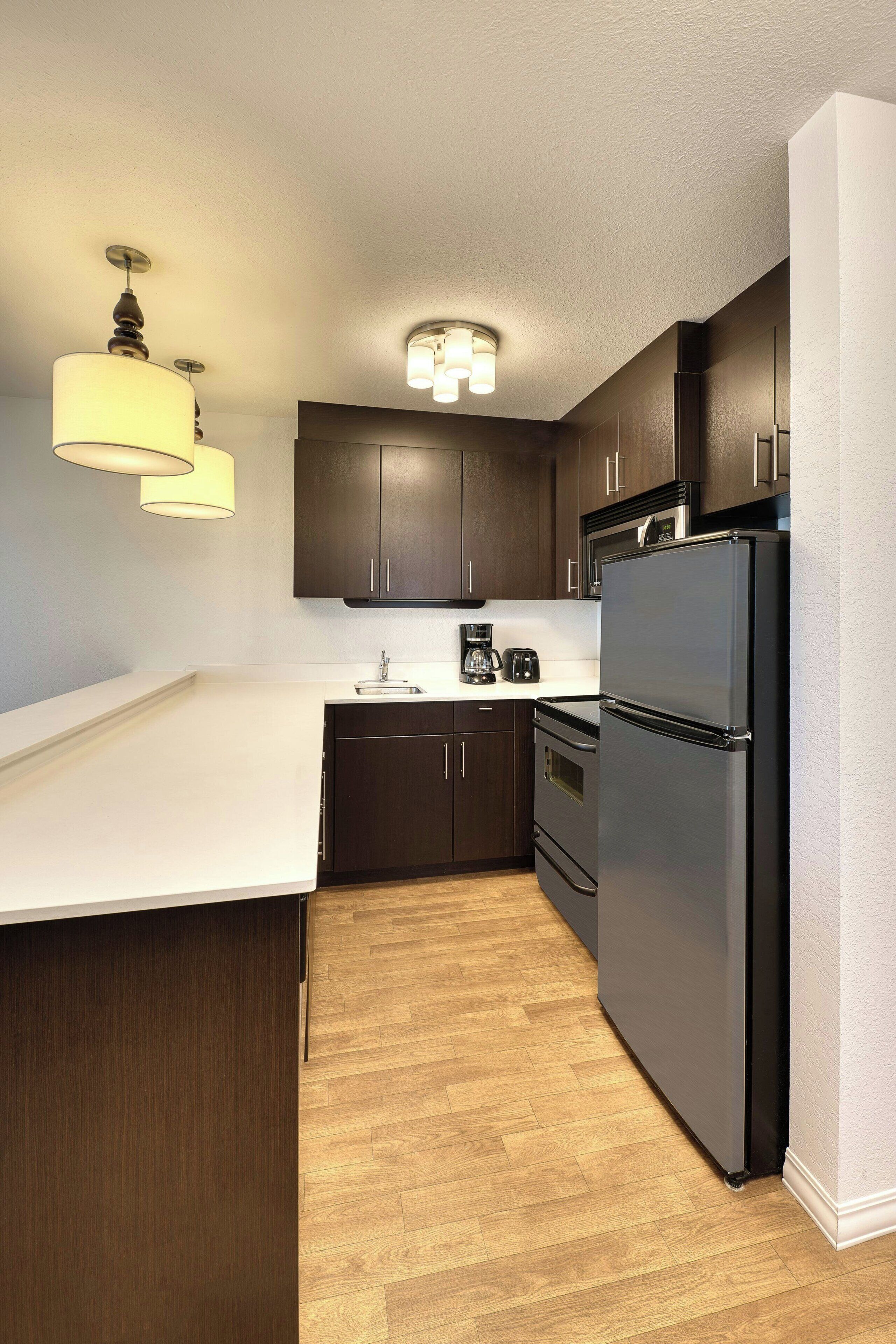 A modern kitchen with dark wooden cabinets, a stainless steel refrigerator, and a white countertop.
