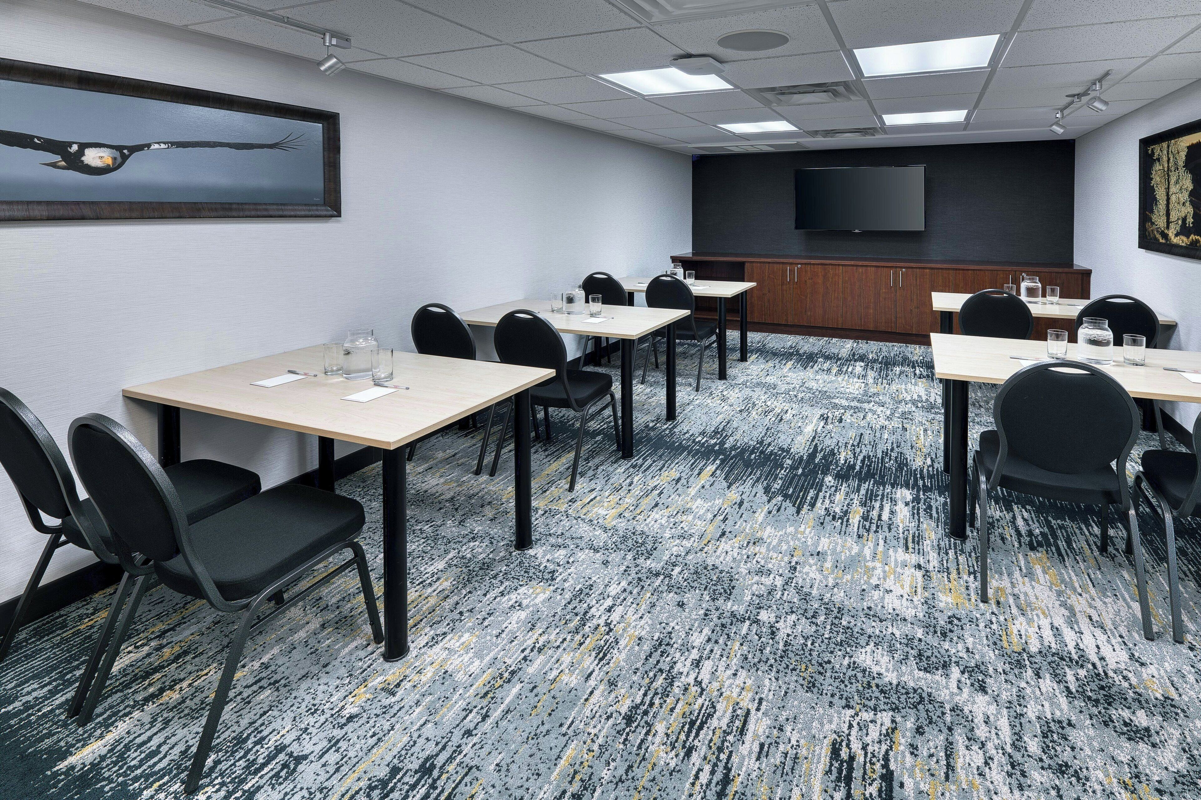 A conference room with multiple tables and chairs, a large flat-screen TV on the wall, and a patterned carpet.