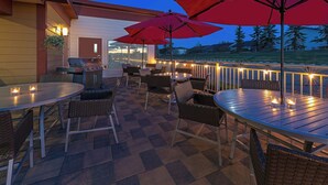 An outdoor patio area with round tables and chairs, red umbrellas, and string lights. - Towneplace Suites by Marriott Red Deer (Red Deer)