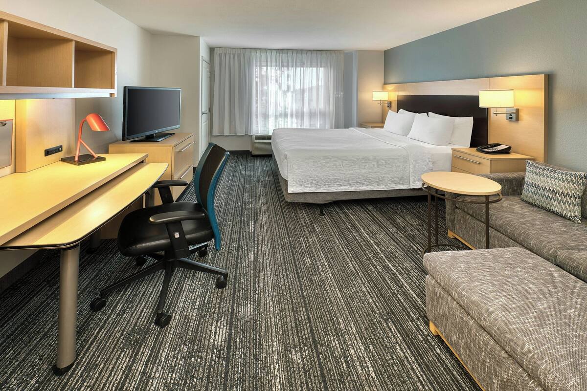 Une chambre d’hôtel équipée d’un lit, d’un bureau, d’une chaise, d’une télévision et d’une petite table ronde.