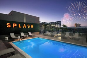 A rooftop pool area with a sign reading "SPLASH," lounge chairs, and a view of fireworks in the background. - SpringHill Suites by Marriott at Anaheim Resort/Conv. Cntr (Anaheim)