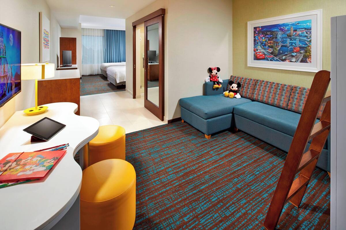 A hotel room with a desk, a sofa, a chair, and a large painting on the wall.