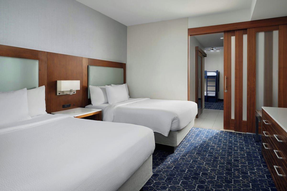 A hotel room with two beds, a nightstand, a wooden headboard, a blue patterned rug, and a wooden wardrobe.