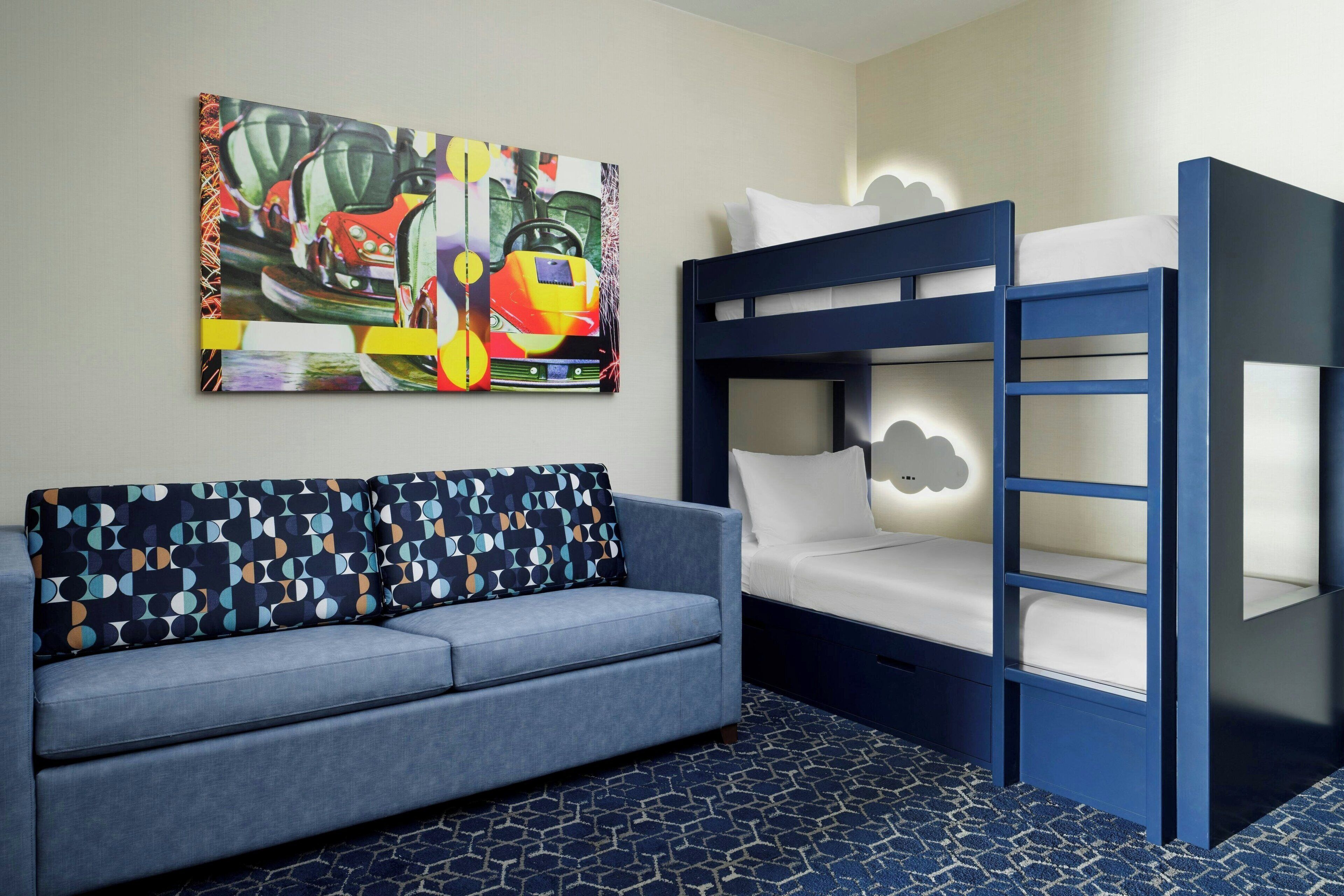 A room with a bunk bed, a sofa, and a colorful abstract painting on the wall.