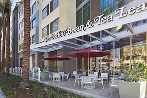 Fachada de The Coffee Bean & Tea Leaf con asientos al aire libre y palmeras.