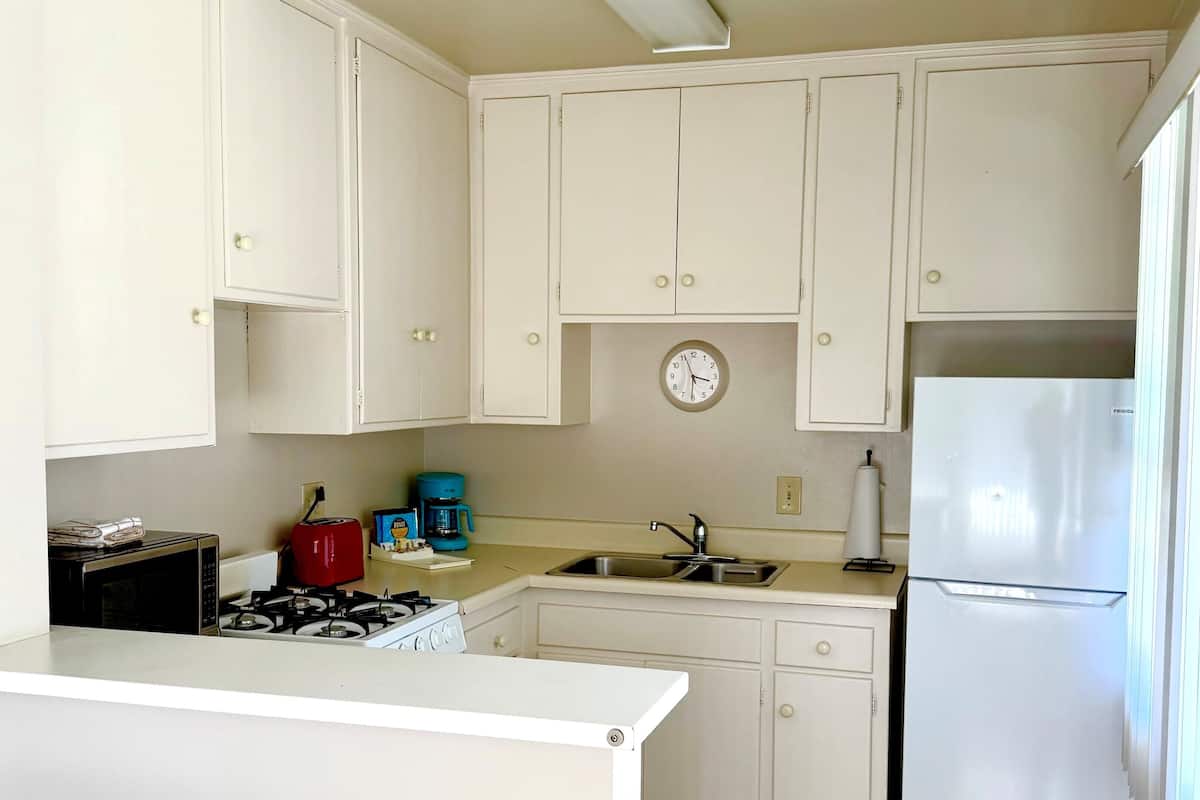 A kitchen with white cabinets, a clock, a stove, a sink, and a refrigerator.