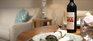 A dining table with a bottle of wine, a glass, a plate with a napkin, and a candle.
