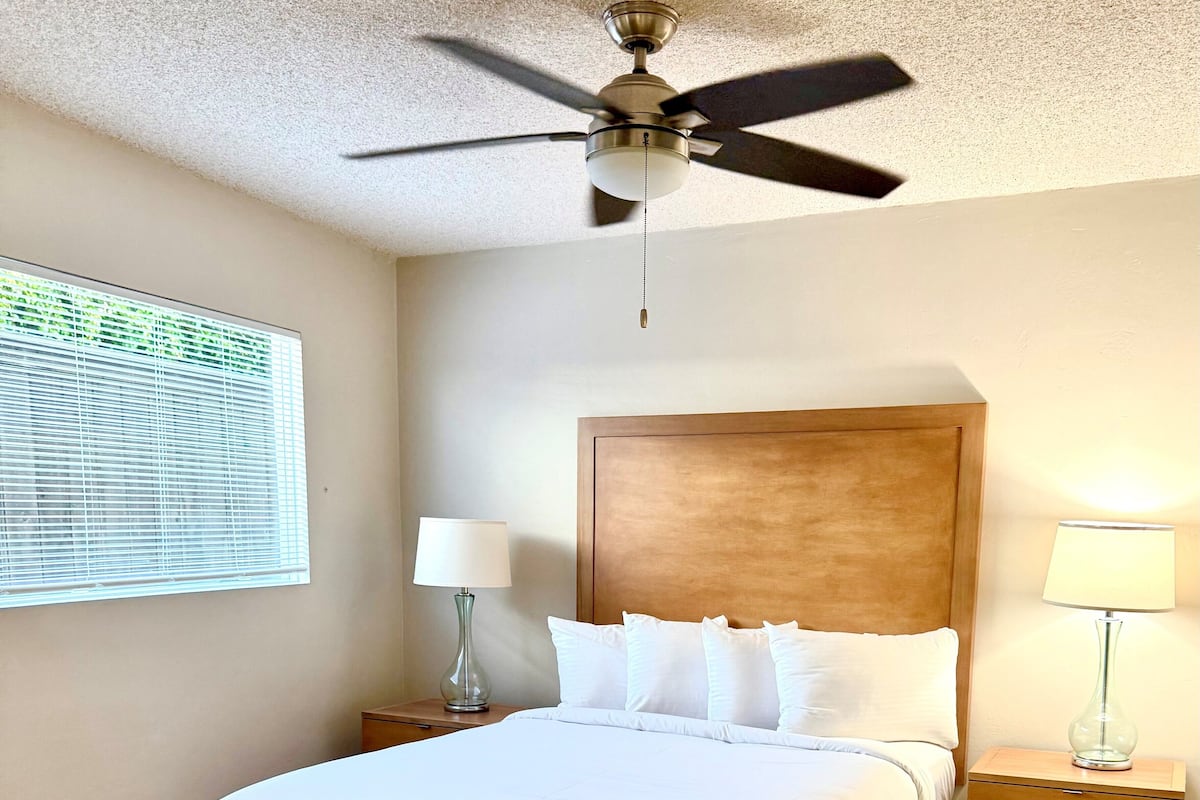A neatly made bed with white linens, a wooden headboard, and a ceiling fan.