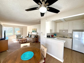 A spacious living area with a dining table, a sofa, and a kitchen with white cabinets and appliances.