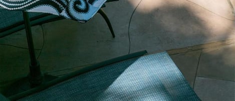 Un patio con una mesa de metal, un banco y un parasol estampado.