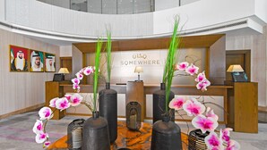 A reception area with a wooden desk, black vases with pink orchids, and a sign that reads "Somewhere". - Somewhere Hotel Apartment (Dubai)