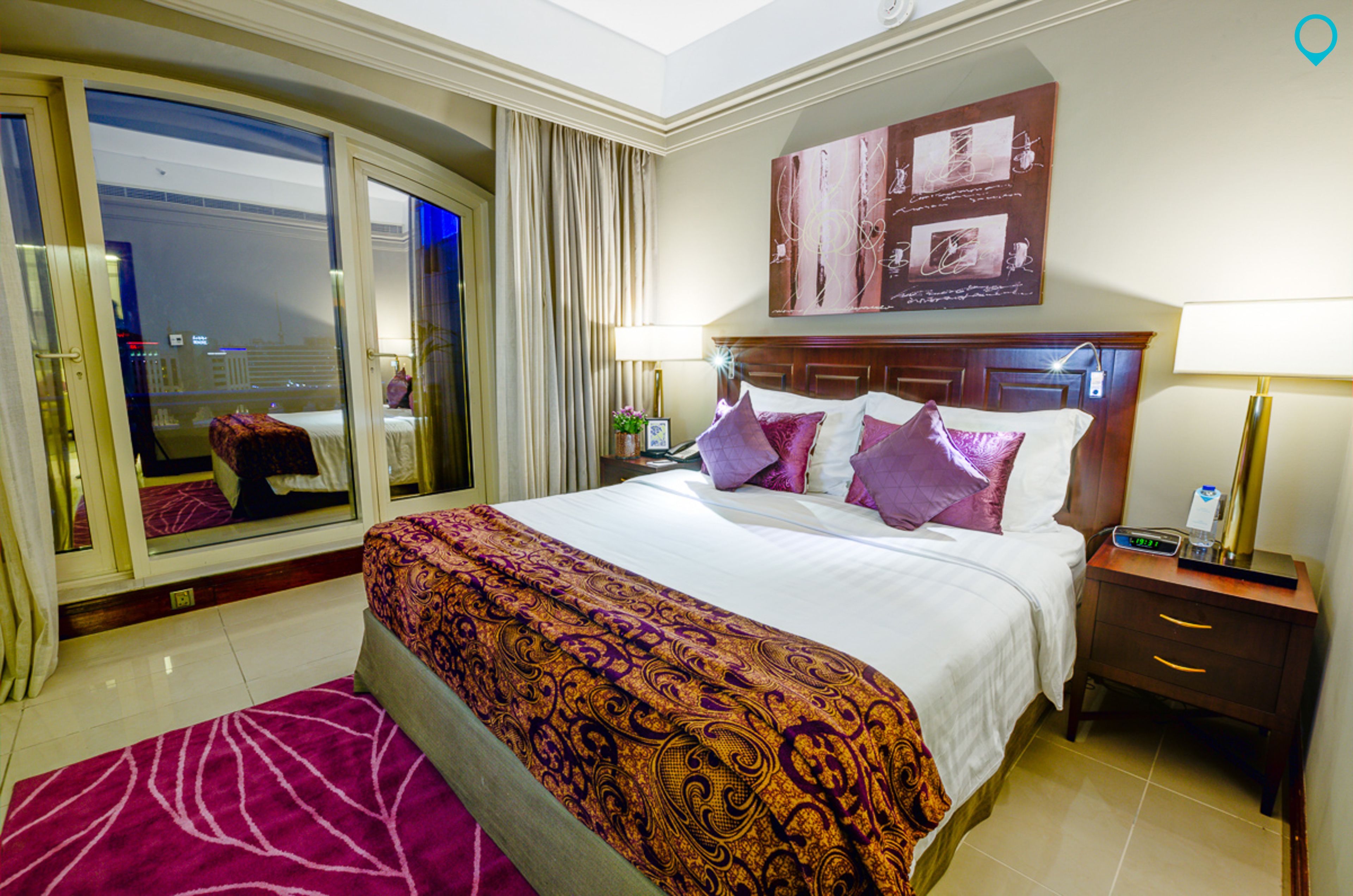 A hotel room with a large bed, a nightstand, a mirror, and a view of the city through the window.