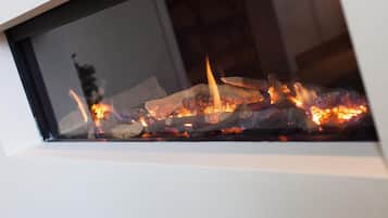 A fireplace with visible logs and flames, set in a white wall with a window above it.