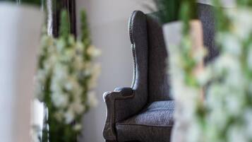 A small, dark-colored armchair in a room with a wooden floor, surrounded by white flowers and greenery.