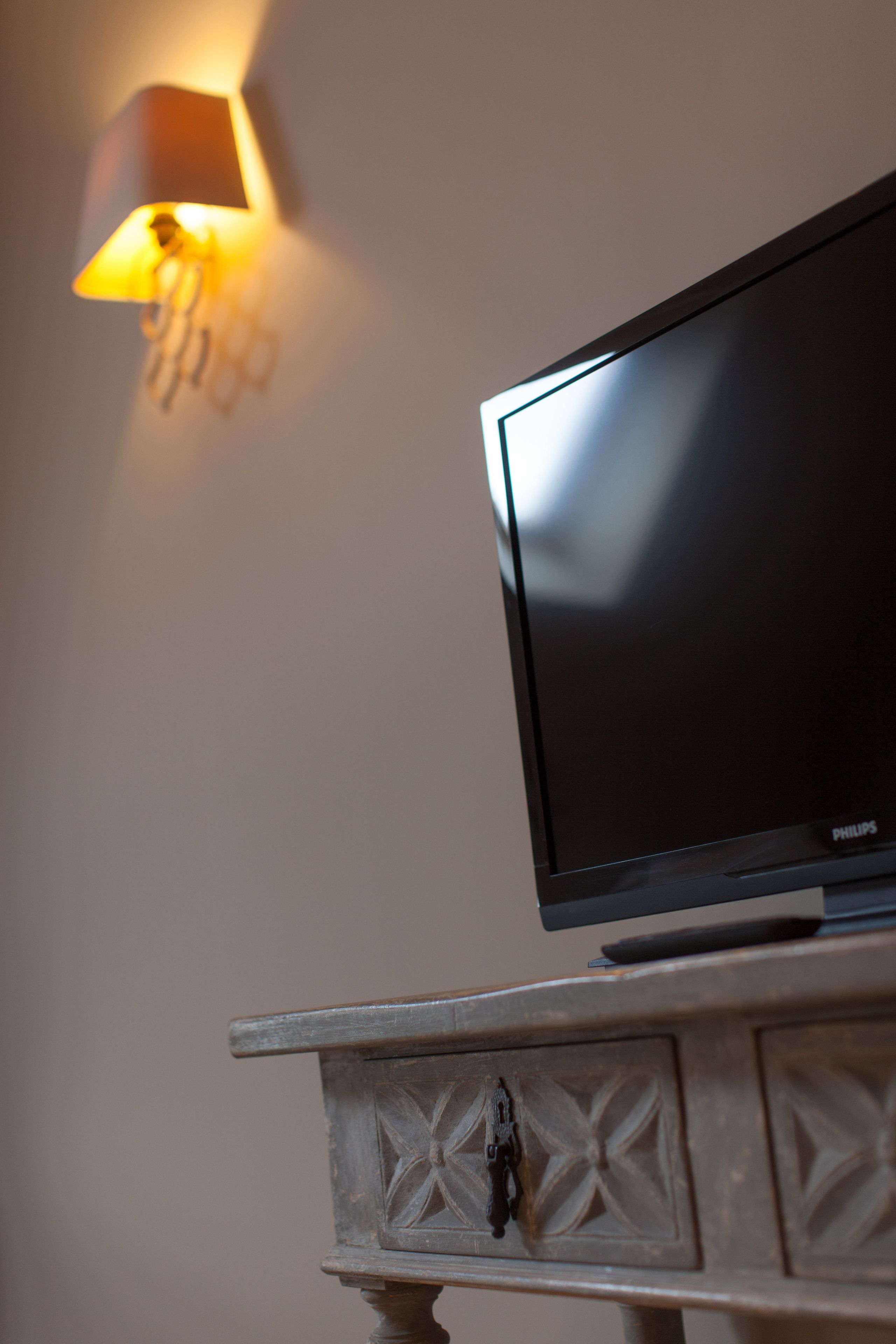 A television on a wooden cabinet with a wall-mounted lamp.
