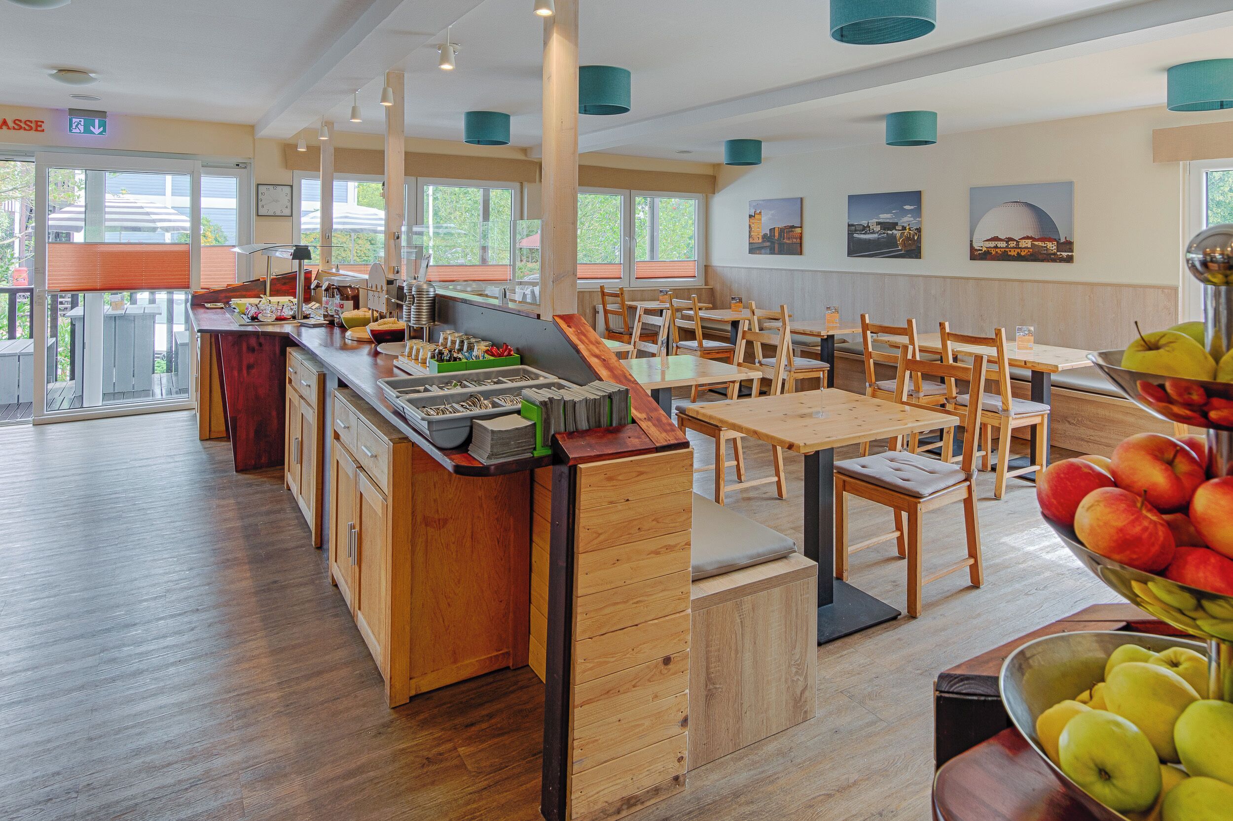 A modern restaurant with wooden furniture, a fruit display, and large windows.