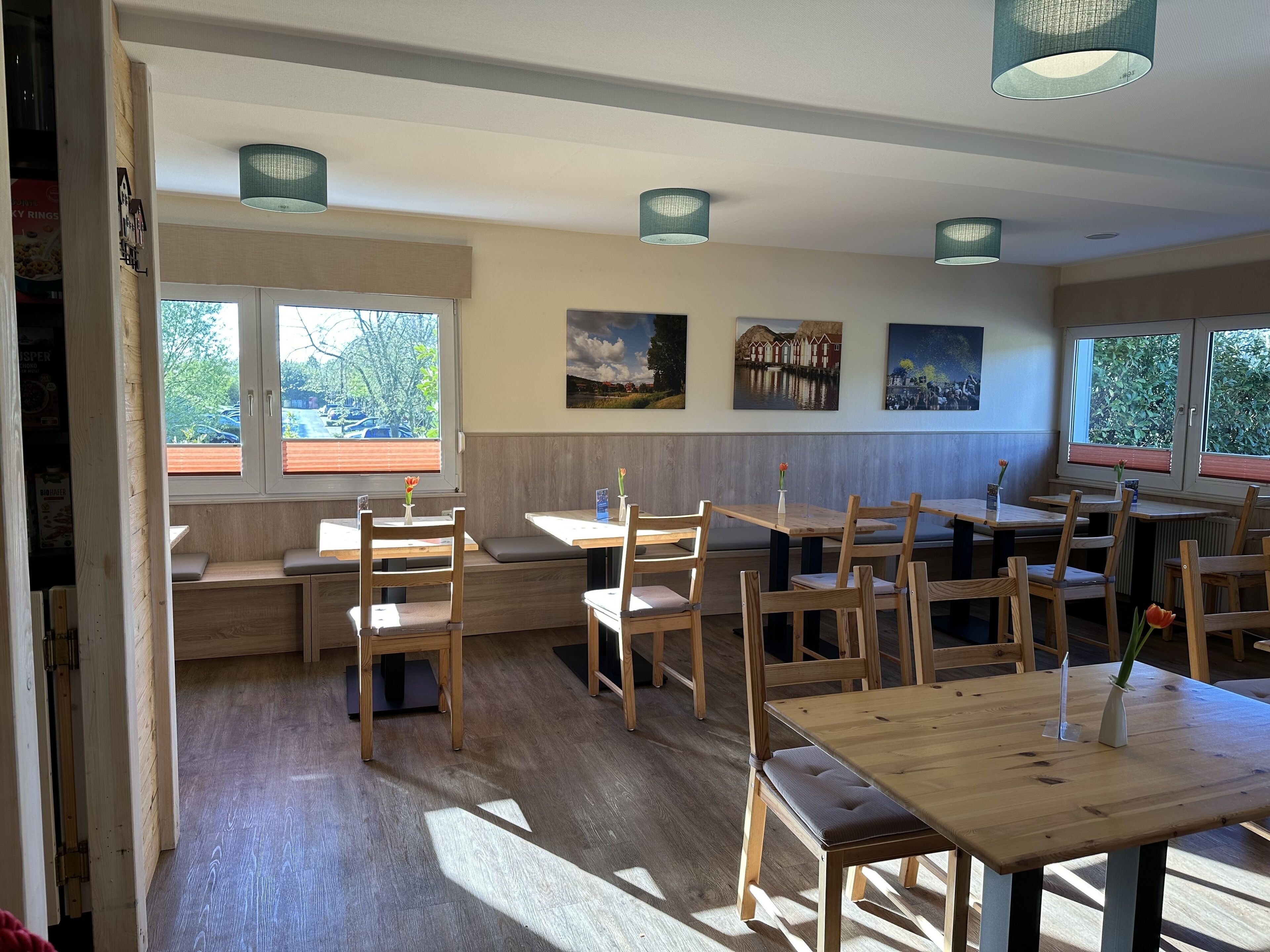 A restaurant with wooden tables and chairs, large windows, and artwork on the walls.
