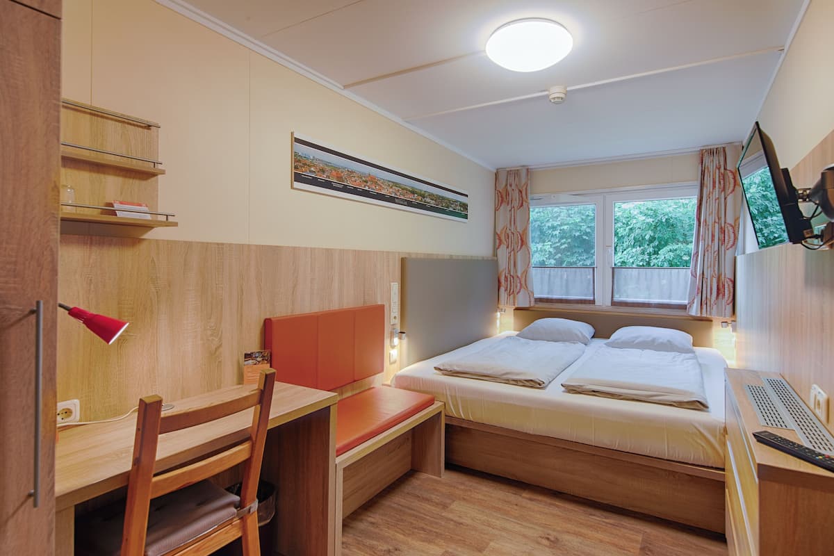 Hotelkamer met een bed, bureau, stoel, televisie en raam met gordijnen.