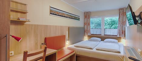 Habitación de hotel con cama, escritorio, silla, televisión y ventana con cortinas.