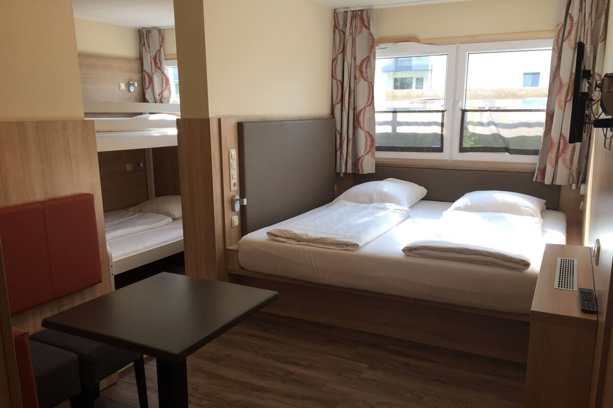 Een kleine kamer met een eenpersoonsbed, een tafeltje en een stapelbed.