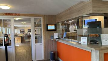 Un espace d’accueil moderne avec un comptoir en bois, un écran numérique et un panneau indiquant le service d’enregistrement rapide.