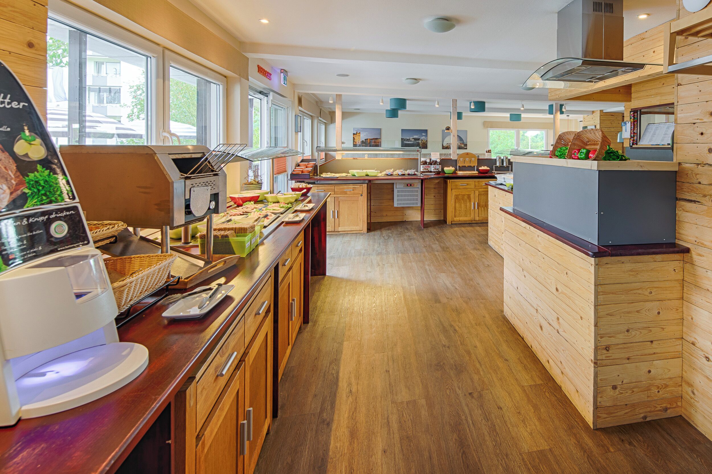 A modern kitchen with wooden cabinets, a coffee machine, and a buffet area with various food items.