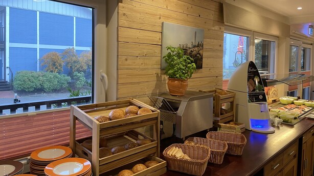 Een buffetruimte met houten kasten, een plant en een presentatie van brood en gebak.