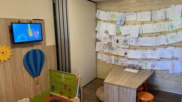 Zona de juegos infantiles con televisor, una pared decorada con dibujos infantiles y una mesa de juegos.