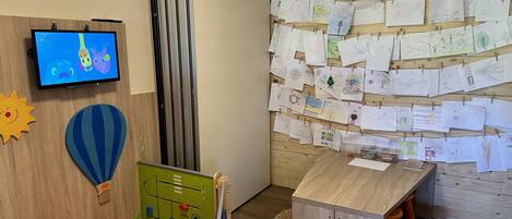 A children's play area with a TV, a wall with children's drawings, and a play table.