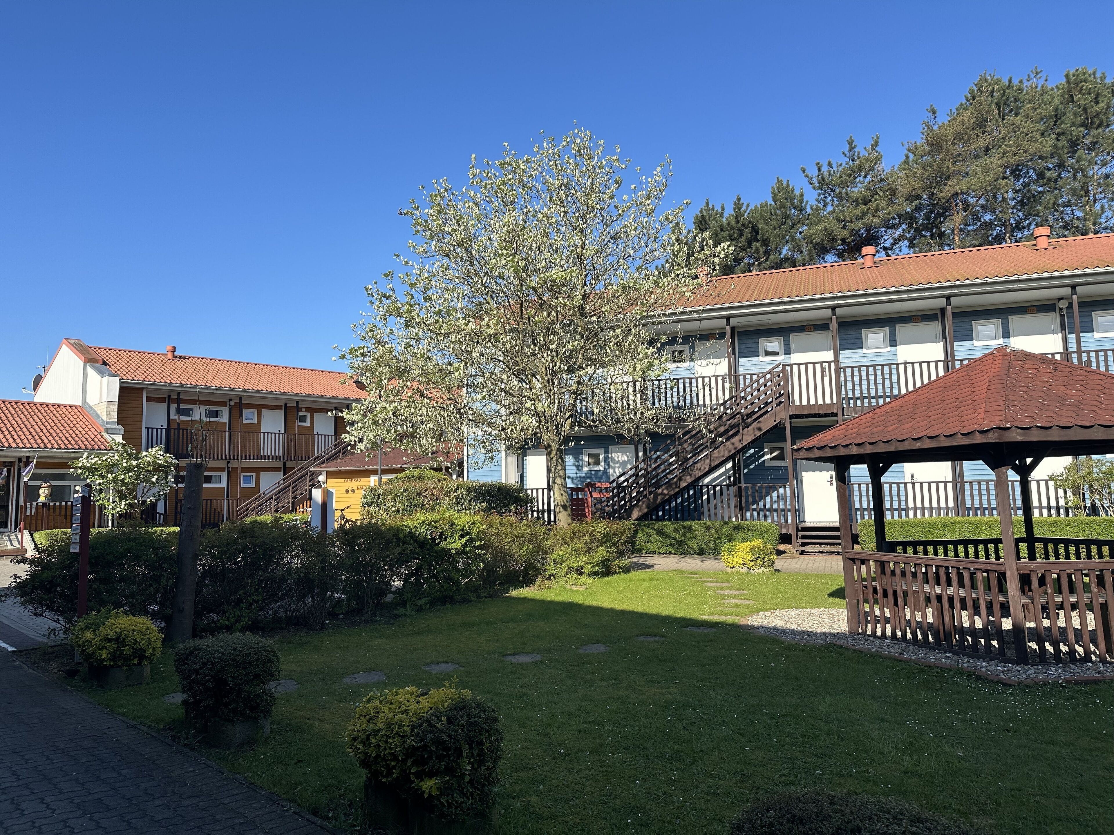 A courtyard with a gazebo, a small tree, and a building with a red-tiled roof.