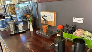 Un bar de café con una máquina de café, un cartel que dice "Kaffee" y diversos objetos relacionados con el café.