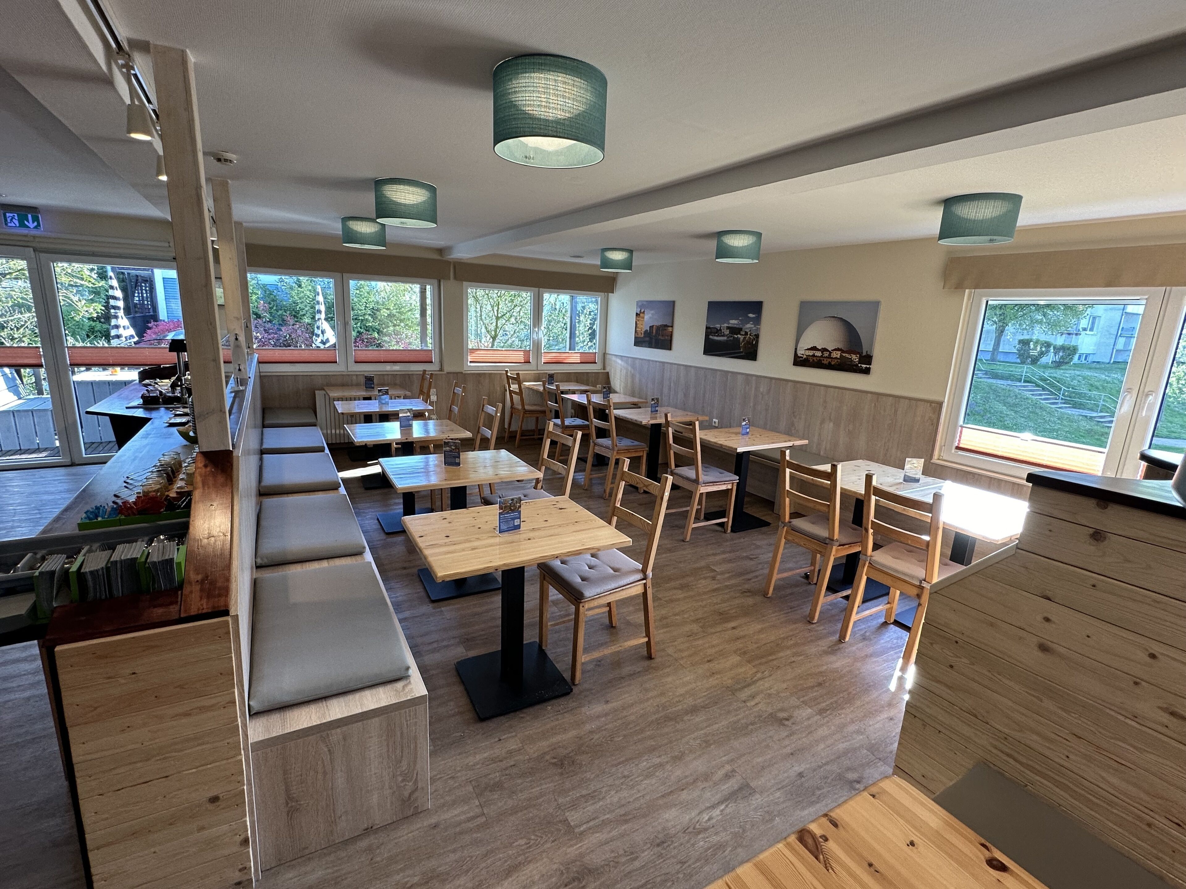 Un restaurant moderne avec des meubles en bois, de grandes fenêtres et des luminaires suspendus.