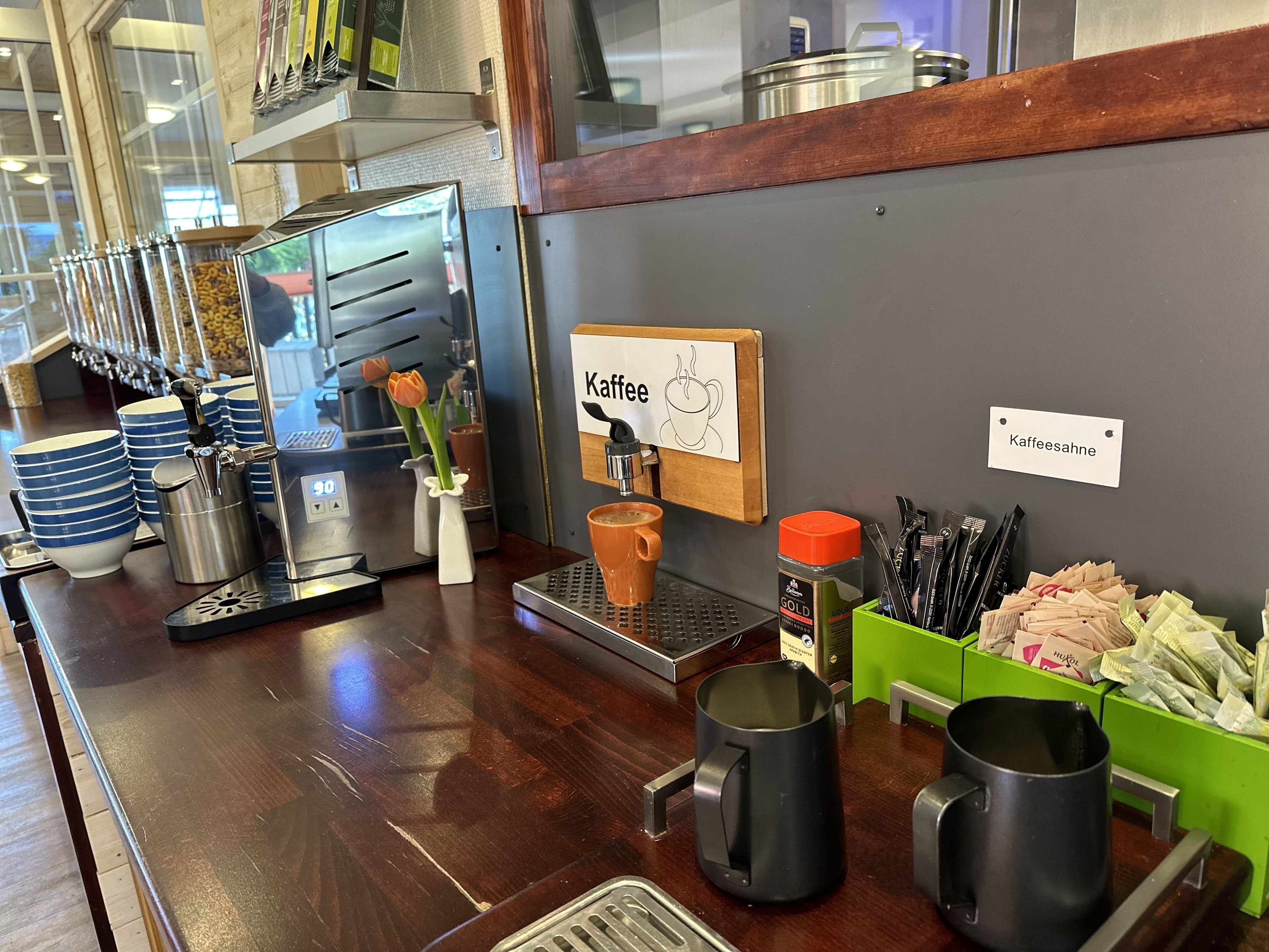 Ein Café mit einer Kaffeemaschine, Tassen und einem Schild mit dem Schriftzug 'Kaffee'.
