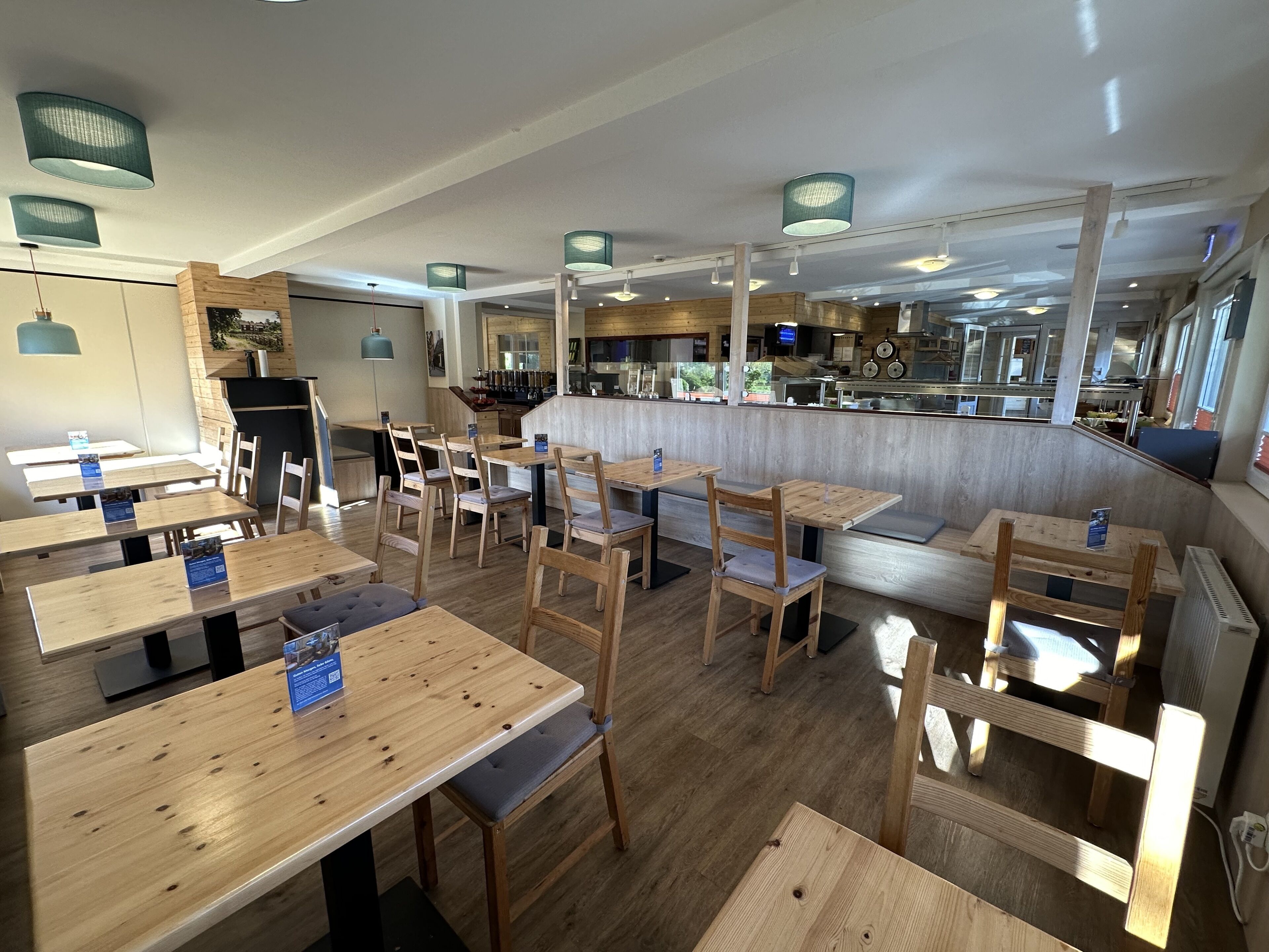 A restaurant with wooden tables and chairs, a bar area, and a kitchen visible through the counter.