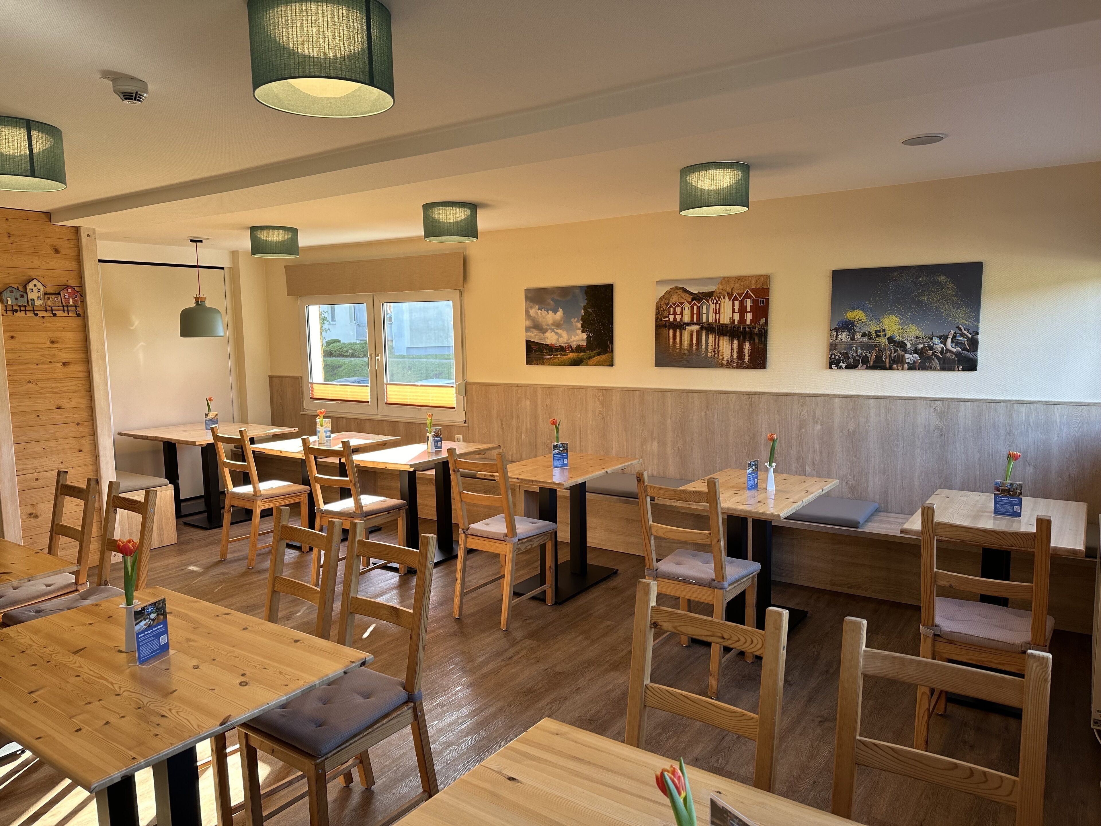 Ein Restaurant mit Holztischen und -stühlen, Pendelleuchten und Kunstwerken an den Wänden.