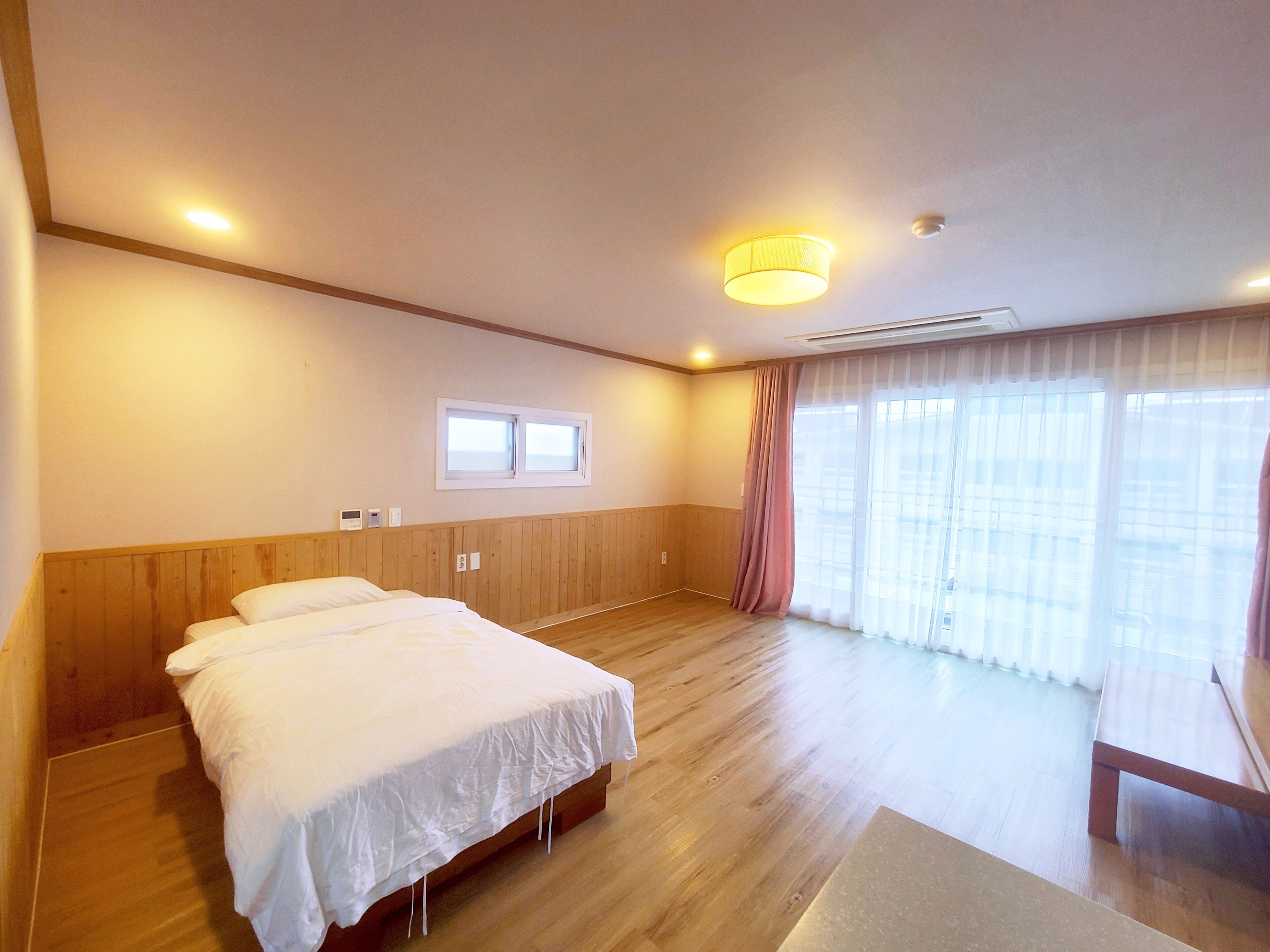 A hotel room with a wooden bed, a small window, and a large window with curtains.