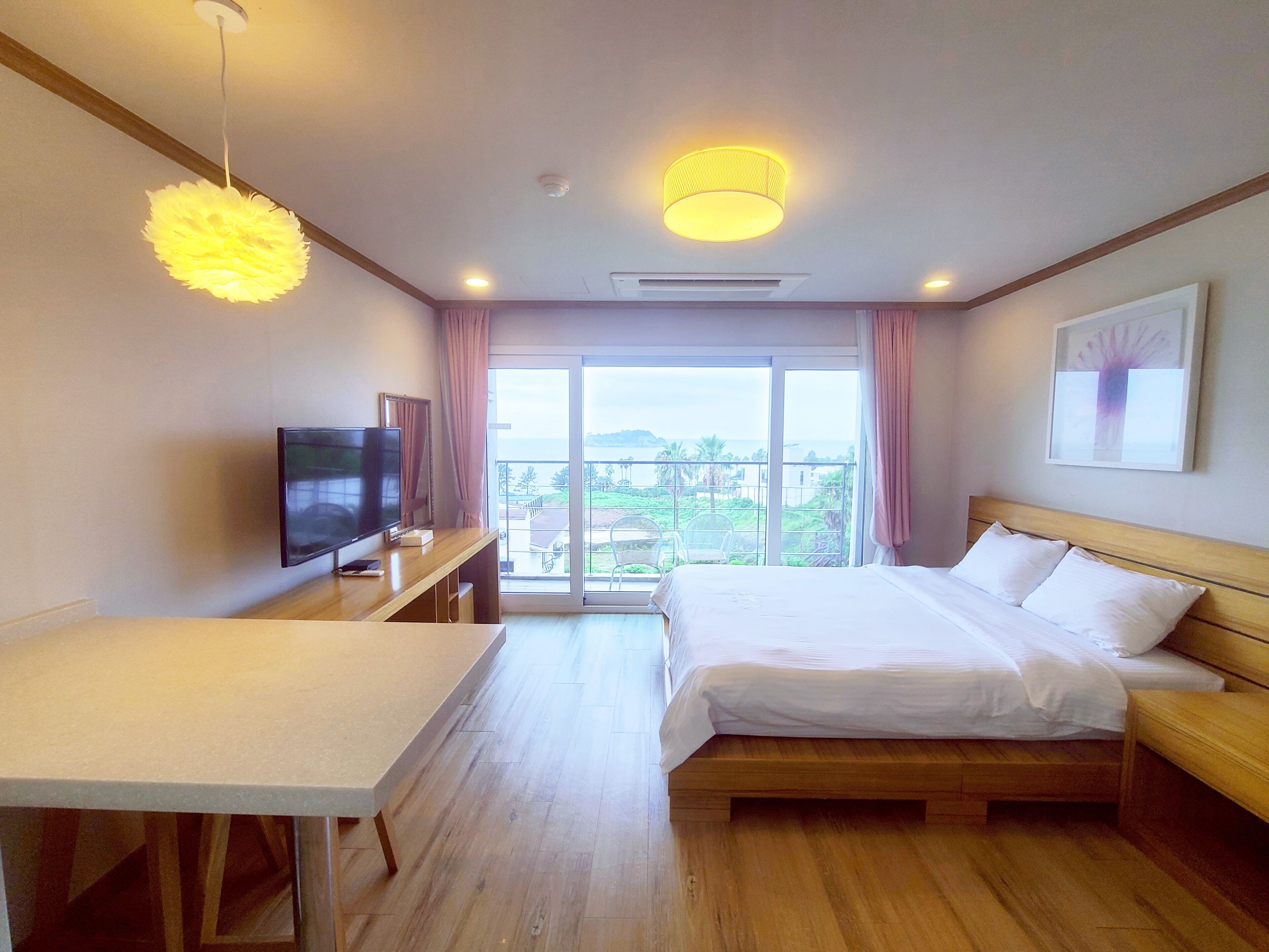 A hotel room with a bed, a TV, a desk, and a balcony with a view.