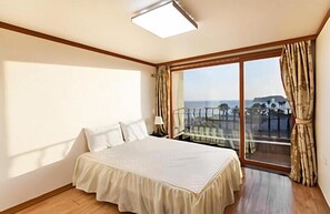 Un dormitorio con una cama grande, una mesita de noche y vista al mar a través de una puerta corrediza de vidrio.