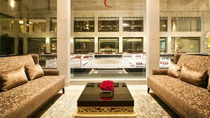 A lobby with two sofas facing a large window, a black coffee table with a red flower centerpiece, and a decorative wall with a red symbol above the window. - The Lalit Traveller Jaipur (Jaipur)