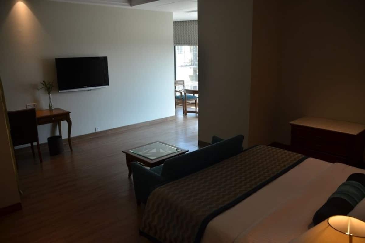 Une chambre d’hôtel avec un lit, un téléviseur fixé au mur, une petite table avec un vase et une vue sur le balcon extérieur.