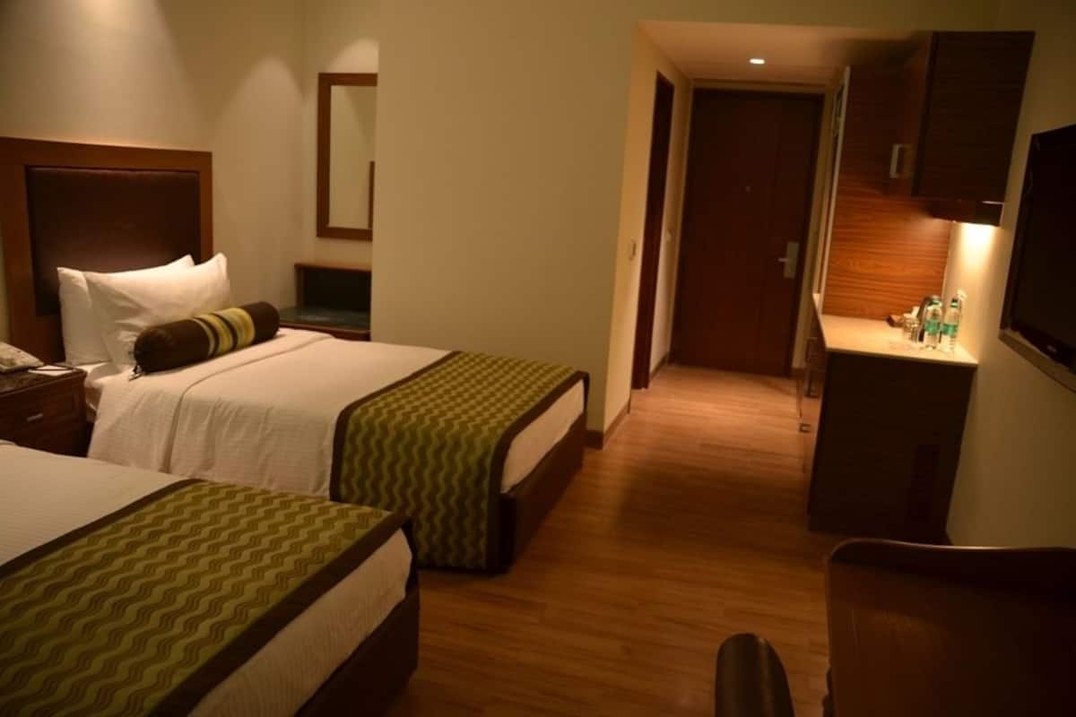 Une chambre d’hôtel avec deux lits, un bureau, un miroir et une télévision.