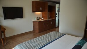 A bedroom with a bed, a TV mounted on the wall, wooden cabinets, and a mirror. - The Lalit Traveller Jaipur (Jaipur)