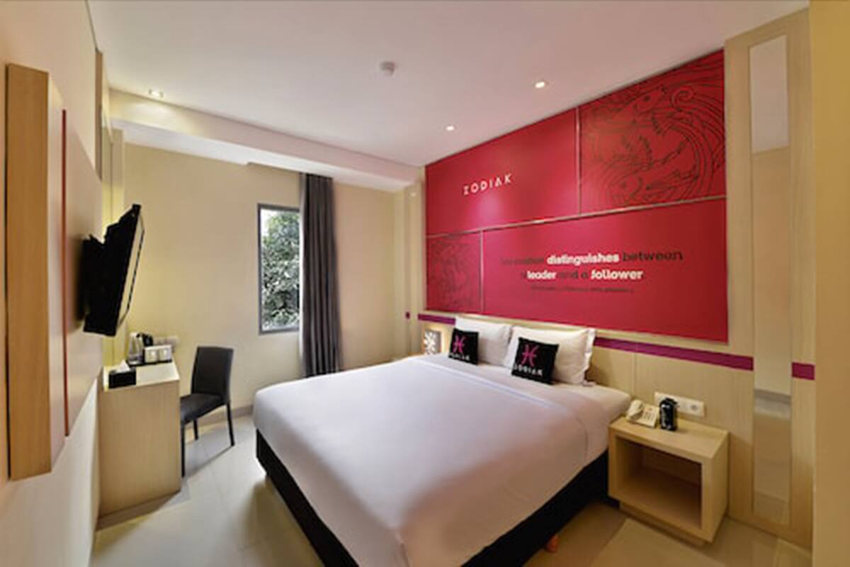 A modern hotel room with a large bed, a desk, a chair, and a TV.