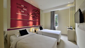 Habitación de hotel con dos camas, un espejo grande, televisión y una cita en la pared.