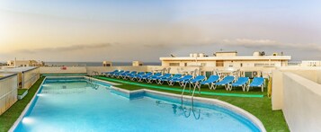 Una piscina al aire libre, sombrillas, sillones reclinables de piscina