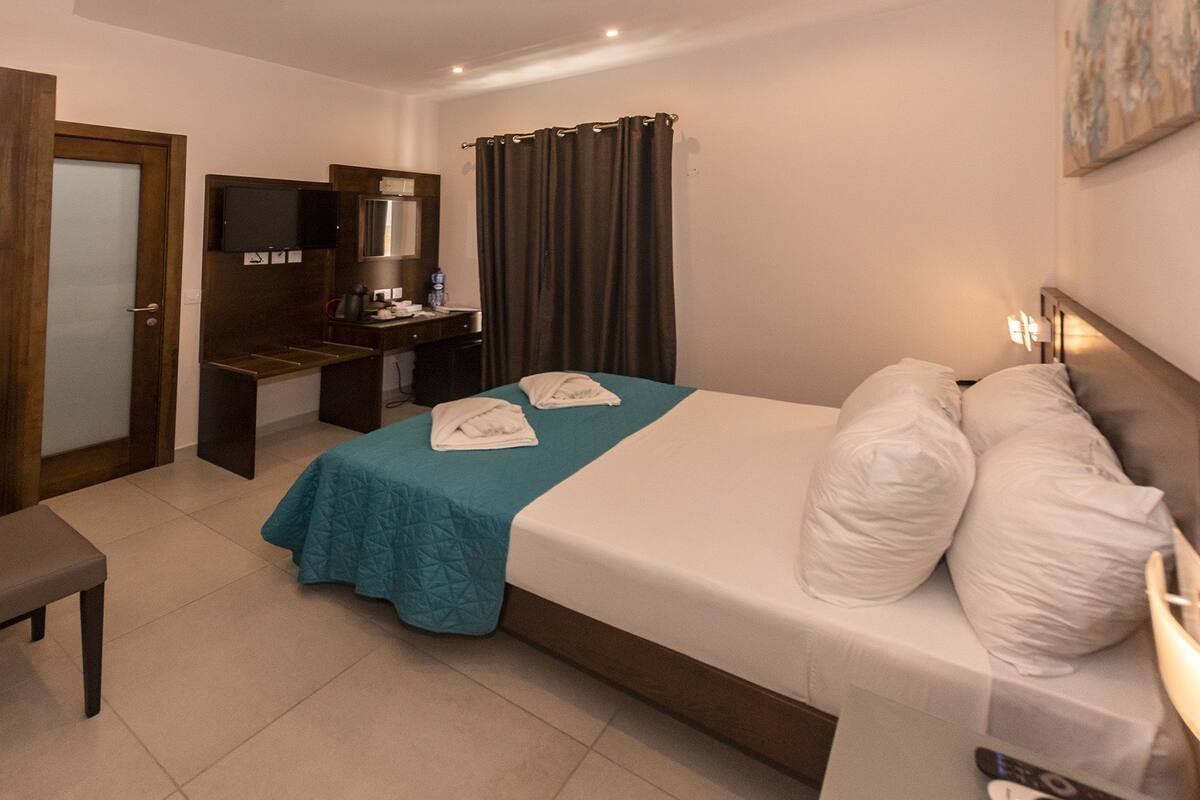 A hotel room with a bed, a desk, a chair, a television, a mirror, and a window with curtains.