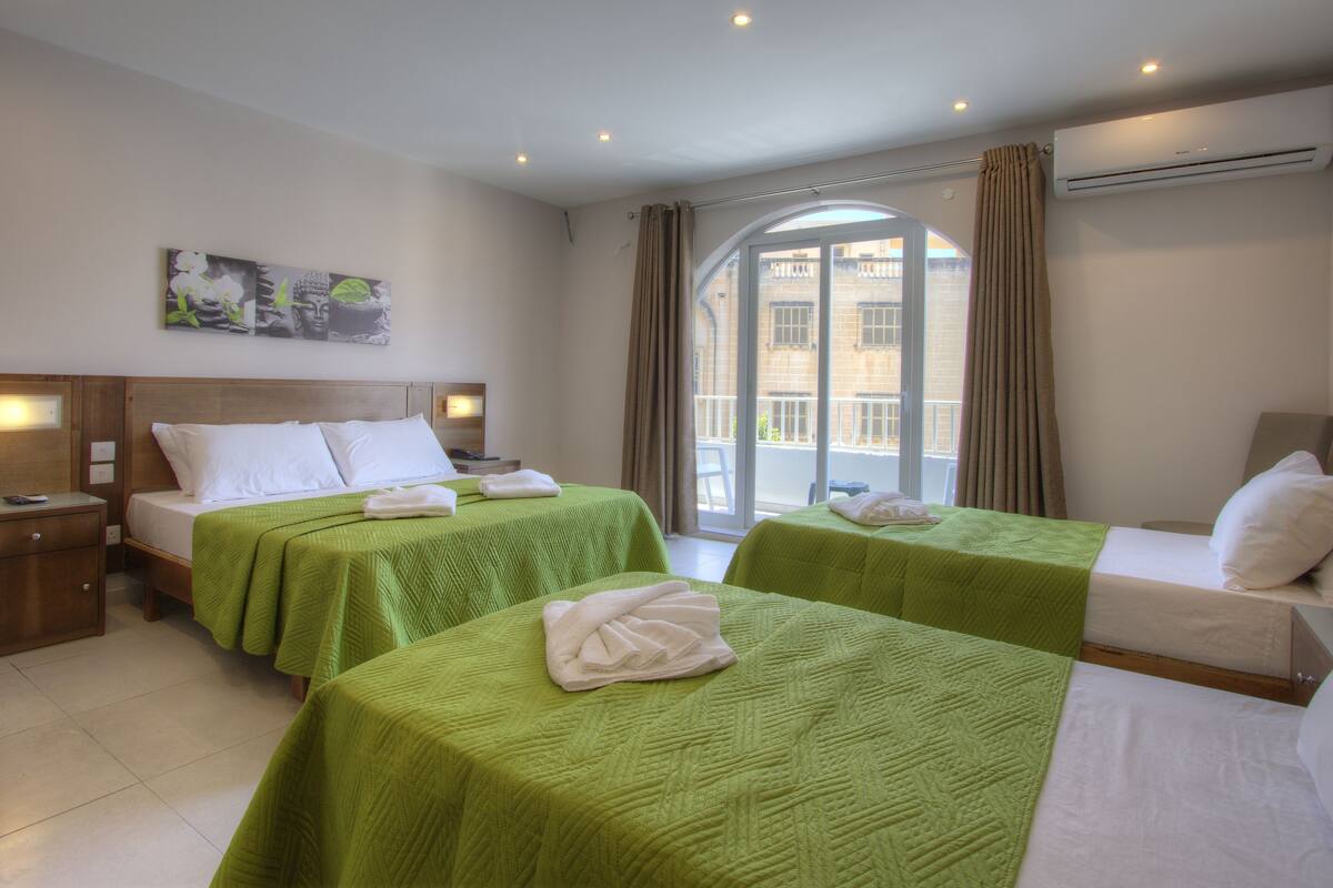 A hotel room with two beds, a large window with curtains, a painting on the wall, and an air conditioning unit.