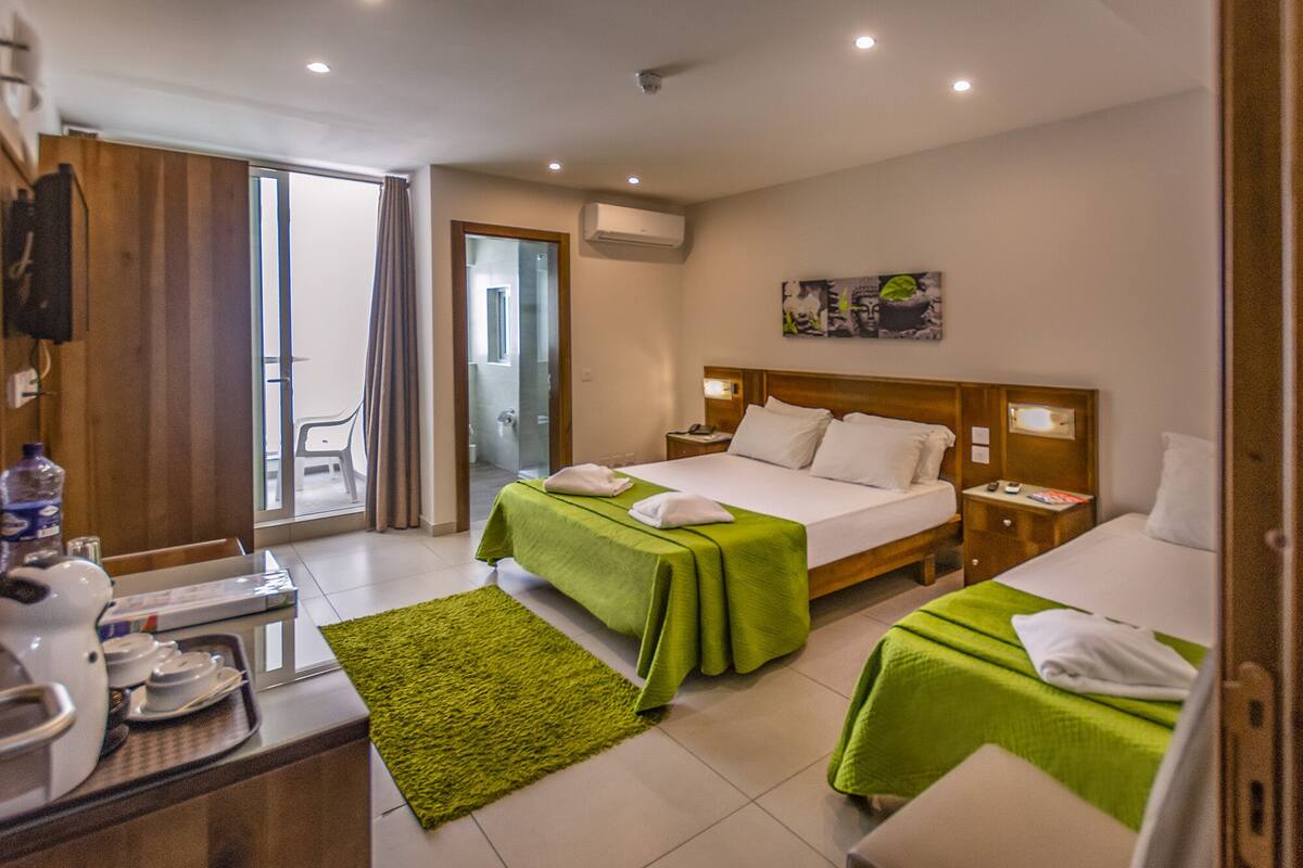 A hotel room with two beds, a desk with a chair, a small table with a water bottle, and a green rug.